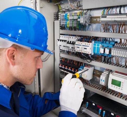 Mannlig elektriker arbeider på sikringsskap med skrutrekker